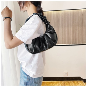 Close-up of black pleated cloud bag with stylish handle held by a model indoors