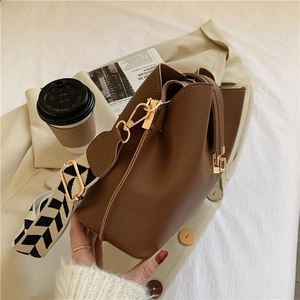 Close-up of brown bucket bag with a geometric pattern wide strap on beige clothing