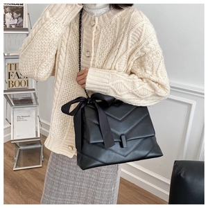 Detail of black quilted leather shoulder bag with a large bow and chain strap on model