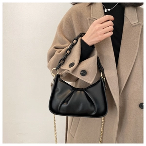 Detail of black pleated cloud bag featuring chunky acrylic chain and gold metal strap