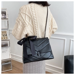 Detail of black quilted shoulder bag with large silk bow and dark metallic chain