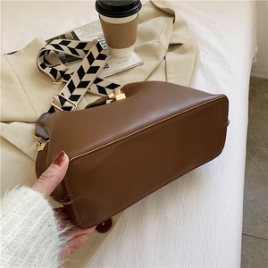 Detail of dark brown leather bucket bag with wide chevron strap on a beige trench coat