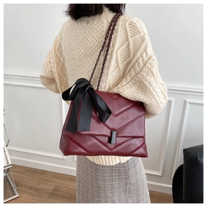 Detail of burgundy quilted shoulder bag featuring a large black bow and chain strap