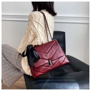 Detail of burgundy quilted bag with V-shaped stitching and a black silk ribbon bow