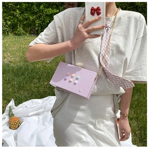 Detail der fliederfarbenen Box-Tasche mit 3D-Blüten und goldener Kette auf Gras