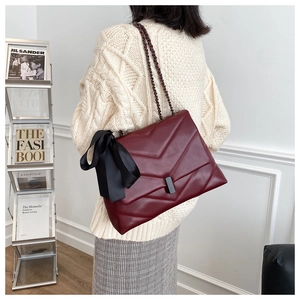 Detail of burgundy quilted chain bag with silk bow charm and metallic lock on a model