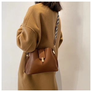 Detail of a brown leather bucket bag featuring a black and white geometric wide strap