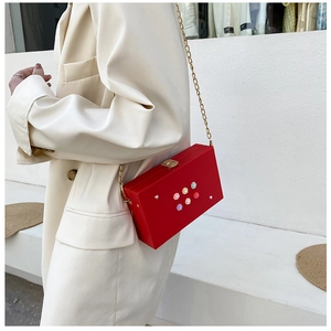 Rote Box-Clutch mit goldener Kette und bunten Blumen auf einem cremefarbenen Blazer