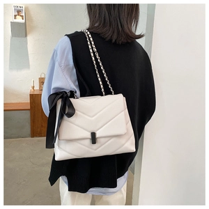 Detailed view of white quilted crossbody bag with black bow and chain strap on a model