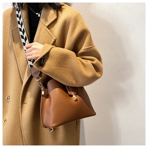 Detail of caramel leather bucket bag featuring a wide patterned strap and gold lock