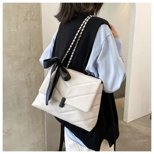 Close-up of white quilted chain bag with a black silk bow shown on a model