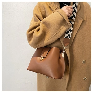 Detail of a brown leather bucket bag featuring a wide geometric woven shoulder strap