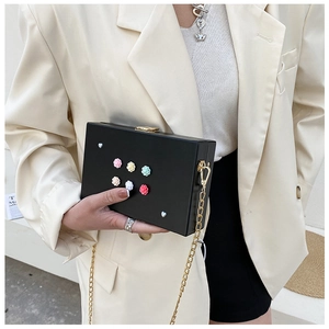 Detail der schwarzen Box-Tasche mit bunten 3D-Blumen und goldener Kette am Modell
