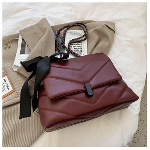 Detail of burgundy quilted chain bag with a large black satin bow on elegant background
