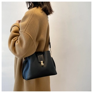 Detail of the black leather shoulder bag with a gold metal clasp worn with a camel coat