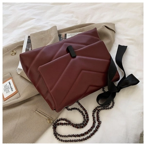 Detail of burgundy quilted chain bag with V-shaped stitching and black ribbon bow