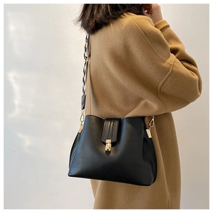 Detail of black bucket bag featuring wide geometric woven strap and gold buckle