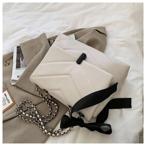 Detailed view of the V-shaped quilting, black metal lock, and silk bow on cream shoulder bag