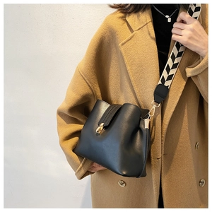 Close-up of black bucket bag with gold clasp and black-white zigzag wide strap on a model