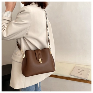 Detail of dark brown bucket bag featuring wide geometric woven strap and gold buckle