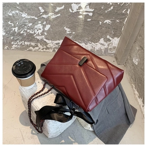 Close-up of wine red quilted leather handbag with chain strap and black ribbon bow