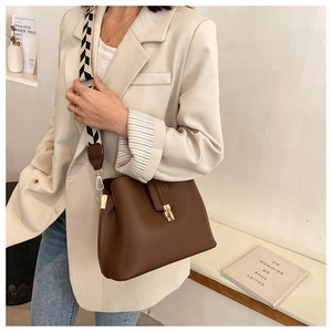 Detail of dark brown bucket bag with geometric strap on a model wearing a blazer