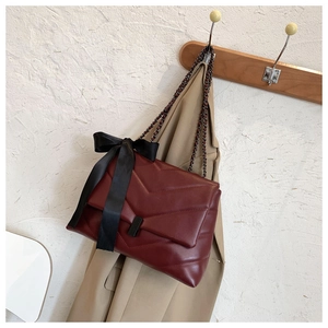 Detail of burgundy V-quilted leather bag with black bow and matte chain strap