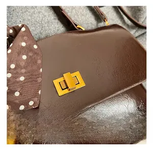 Detail of a dark brown glossy bag featuring a gold metal clasp and a polka dot silk scarf