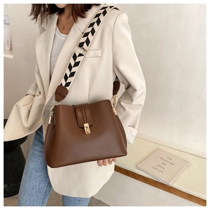 Detail of dark brown leather bucket bag featuring a black and white geometric wide strap