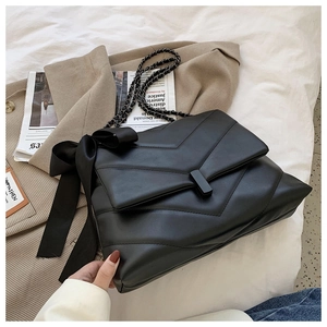 Detail of black chevron quilted leather bag featuring a large silk bow and chain strap