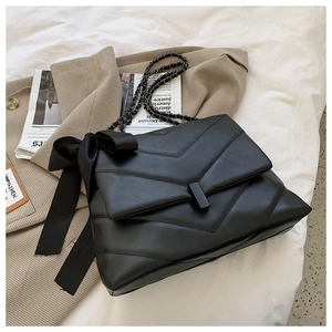 Detail of black quilted shoulder bag with V-shaped stitching and ribbon bow accent