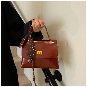 Detail of burgundy leather crossbody bag with silk scarf handle and gold bell charm
