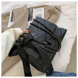 Detail of black quilted shoulder bag featuring side bow and metal chain strap