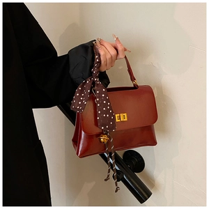 Close-up of a retro reddish-brown leather handbag with a gold lock and silk scarf detail
