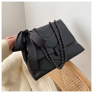 Close-up of matte black V-quilted chain shoulder bag with oversized satin bow detail