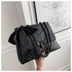 Detail of black chevron quilted tote bag featuring a large satin bow and chain strap