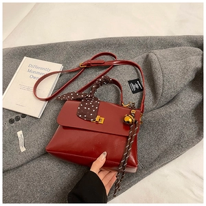 Detail of burgundy glossy handbag with gold buckle and silk scarf on handle