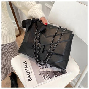 Detail of black quilted shoulder bag with chain strap and oversized decorative bow