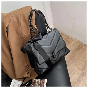 Detail of black quilted leather shoulder bag with large satin bow and chain strap