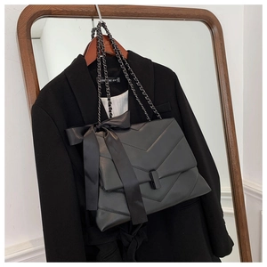 Detail of black quilted shoulder bag featuring a satin bow and metallic chain strap