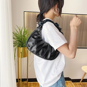 Minimalist black pleated cloud bag made of soft PU leather worn as an underarm shoulder bag