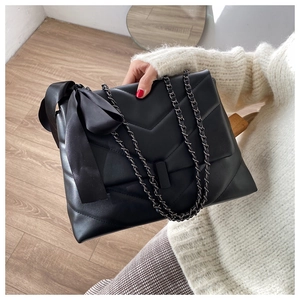 Macro shot of V-quilted faux leather texture and large velvet bow detail on a black bag