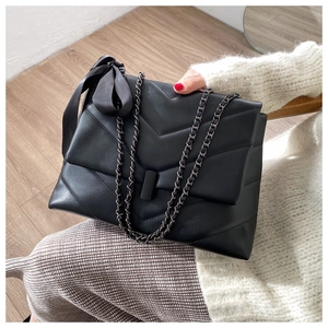 Detail of black quilted chain bag featuring a decorative satin bow and metal lock