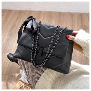 Close-up of black quilted leather bag with V-pattern stitching and velvet bow detail