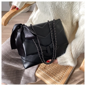 Close-up of black quilted chain bag with V-shaped stitching and side satin bow detail
