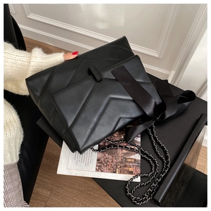 Detail of black chevron quilted shoulder bag with silk bow and metal chain strap