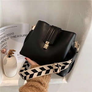 Chic black bucket bag with a chevron woven strap and gold hardware in a minimalist setting