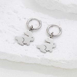 Minimalist silver rabbit charm hoop earrings on a white textured stone background