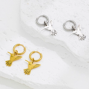 Polished stainless steel hummingbird dangle earrings in gold and silver set on marble
