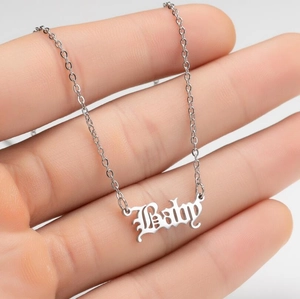 Makro-Detailansicht der silbernen Baby-Halskette mit gotischer Schrift auf der Hand
